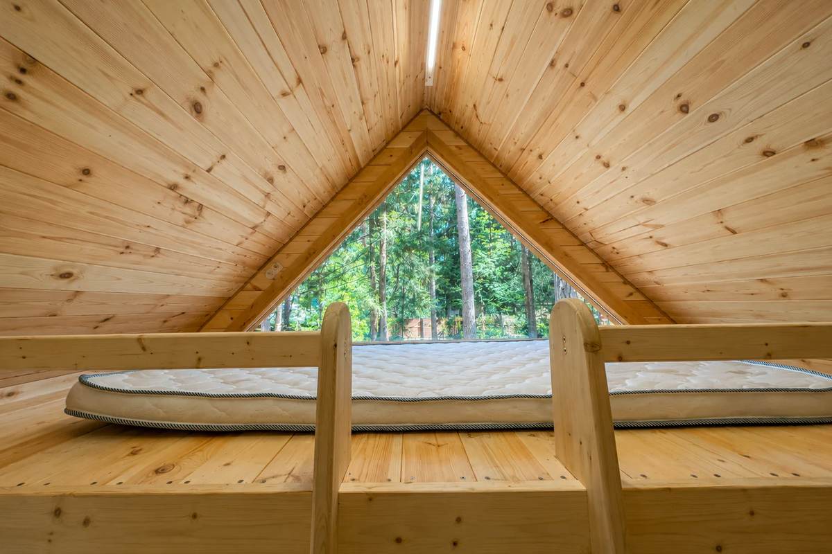 Спальное место под скатом крыши с треугольным окном в дом на дереве